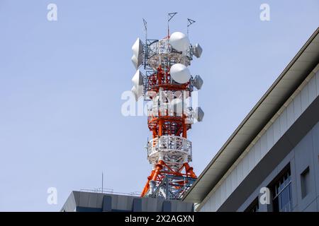 a large red and white mast on a roof with antennas and satellite dishes in front of a blue sky Stock Photo