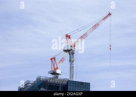 two large red and white cranes on the top of a skyscraper against a blue sky Stock Photo