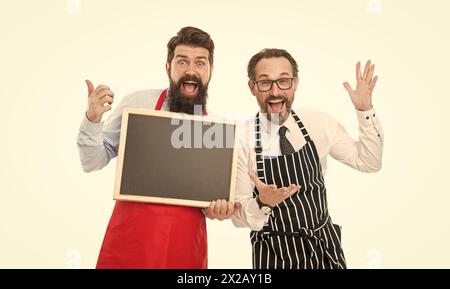 Men bearded informing. Men bearded bartender in apron hold blank chalkboard. Bartender with blackboard advertisement. Hipster bartender show Stock Photo