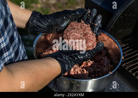 Hands with gloves preparing cooked beef patty burgers on grill and smoker Stock Photo