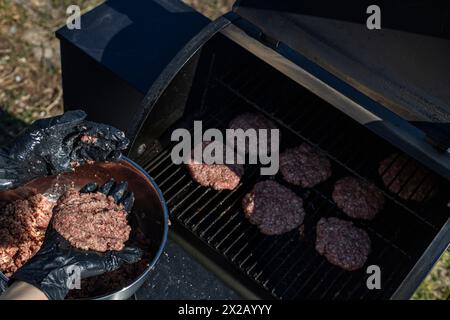Hands with gloves preparing cooked beef patty burgers on grill and smoker Stock Photo