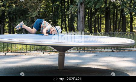 A cheerful and mischievous boy is playing pranks in a city park on a balance disc. Stock Photo