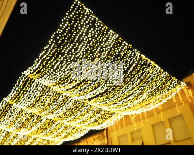 Hanging garlands against the background of the night sky. Festive decoration of city streets. Garlands of yellow, white and gold lights and bulbs. Bea Stock Photo