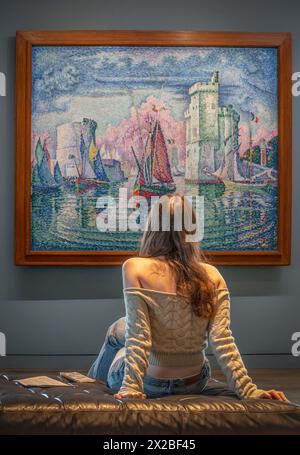 Paris, France - 04 12 2024: Orsay Museum. A girl sitting and looking at the painting Entrance to the Port of La Rochelle painted by Paul Signac Stock Photo