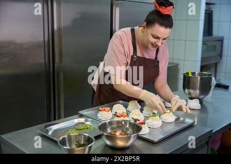 Smiling woman confectioner garnishing cakes with fresh fruits and berries Stock Photo