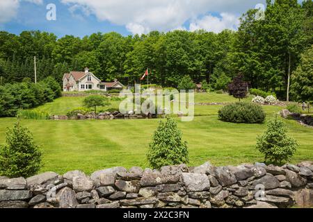 Tan with white trim 1990s contemporary Victorian style country home with storage shed and backyard garden with pond in late spring. Stock Photo