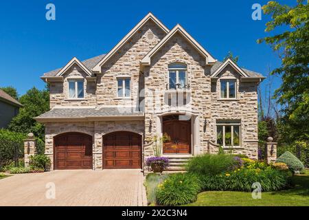 Two story beige, brown and tan cut stone with tan trim luxurious house facade with shrubs and flowers in border. Stock Photo