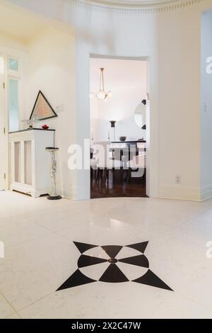 Circular entrance hallway with black  arrow marks design inlaid in white marble floor and view of dining room through doorway inside a 1924. Stock Photo