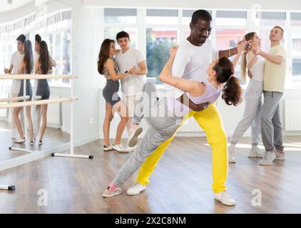 Smiling young woman wearing sportswear dancing in couple samba dance with african american partner during group class at dance salon Stock Photo