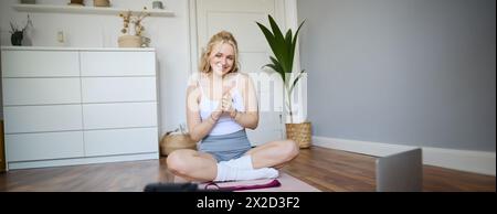 Portrait of young charismatic fitness trainer, girl blogger records video on digital camera, talks about health and workout, doing exercises on rubber Stock Photo
