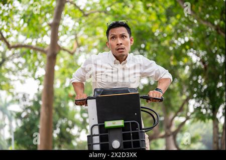 A stressed, anxious Asian millennial businessman is in a hurry to get to work in the morning, riding a bike, concerned about being late, showing urgen Stock Photo