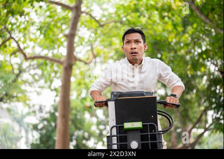 A stressed, anxious Asian millennial businessman is in a hurry to get to work in the morning, riding a bike, concerned about being late, showing urgen Stock Photo