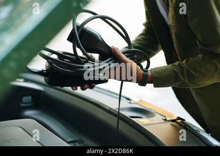 Closeup image of electric car driver putting charging cable in trunk Stock Photo