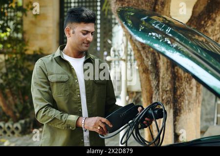 Smiling Indian man putting charging cable in car trunk Stock Photo
