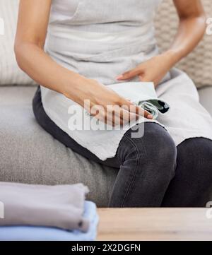 Woman, hands and folding with laundry on sofa for clean clothing, chores or housekeeping at home. Closeup of female person, cleaner or maid with dry Stock Photo