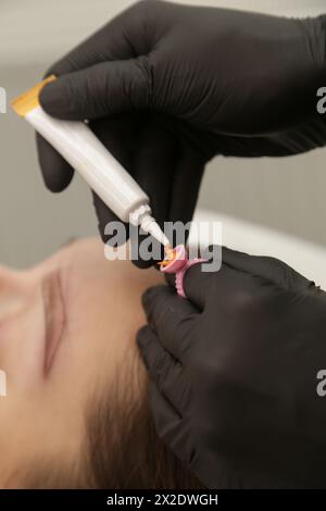 Microblading artist in a black gloves mixing pigment in ink ring cup. Close-up of pigment ring container and ink for eyebrow tattoo. Beauty procedure Stock Photo