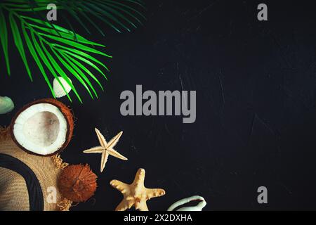 Straw hat, coconut, starfish, palm leaves and seashells on a black background. Summer background, free space for decoration, flat lay. Stock Photo