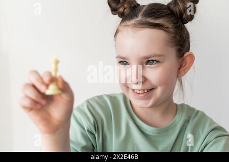 A little girl with a big smile holds a chess piece white queen in her hands. Selected focus. High quality photo Stock Photo