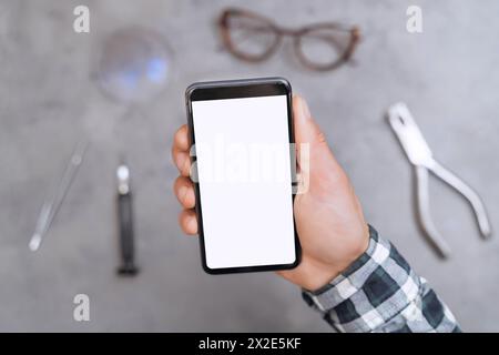 Smartphone with blank screen for text, location, advertisement in hand of optician technician on optical store background with special tools and glasses on table, eyesight and promotion concept Stock Photo