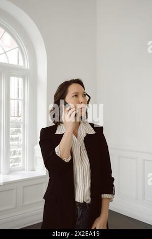 Half-Asian woman talks on phone in business casual attire Stock Photo