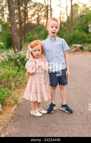 Red haired girl and brother stand on path by flowers Stock Photo