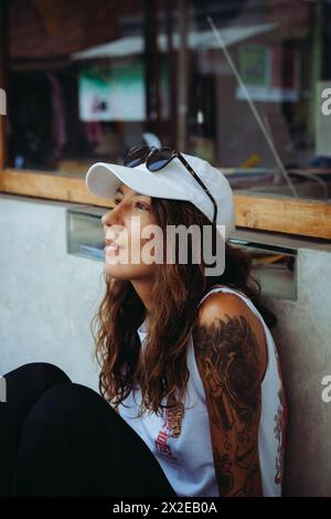 Young smiling tattooed woman sitting on a bench, street photo. Stock Photo