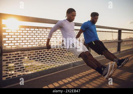 Two african-american friends are exercising on the bridge in the city. They are doing reverse push-ups. Stock Photo