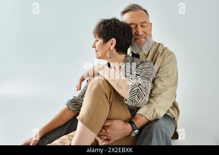 A middle-aged man and woman in stylish attire sit intertwined, creating a visually striking composition in a studio setting. Stock Photo