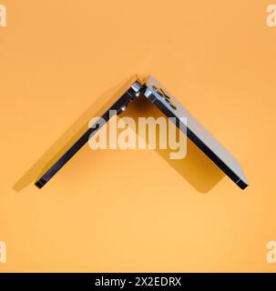 London, United Kingdom - Sep 29, 2022: Apple's titanium-made smartphones, the 13 Pro and 14 Pro, are creatively arranged to form a rooftop shape against an orange background Stock Photo