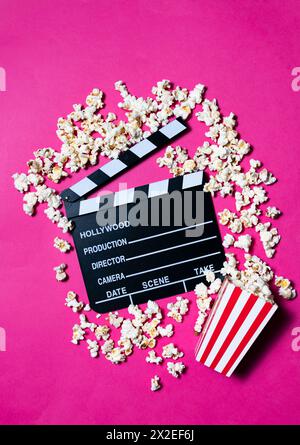 Movie clapperboard and popcorn on fuchsia pink background Conceptual of cinema, entertainment, audiovisual Stock Photo
