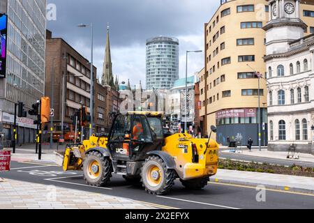 JCB Loadall heavy duty forklift truck passes with a view looking towards the Rotunda in the city centre on 17th April 2024 in Birmingham, United Kingdom. The Rotunda is Birminghams most iconic building, a cylindrical high rise building which is Grade II listed. It is 81 metres tall and was completed in 1965. Refurbished between 2004 and 2008 by Urban Splash with Glenn Howells who turned it into a residential building with serviced apartments on the 19th and 20th floors. The building was officially reopened on 13 May 2008. Stock Photo