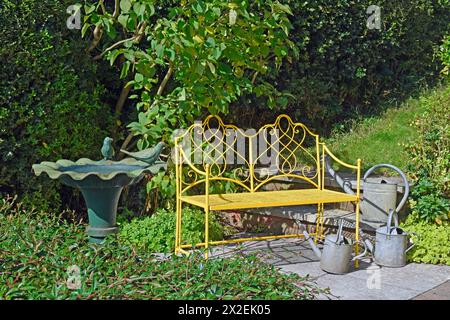 botany, Yellow ornate metal bench in a garden setting with metal bird bath and watering cans, ADDITIONAL-RIGHTS-CLEARANCE-INFO-NOT-AVAILABLE Stock Photo