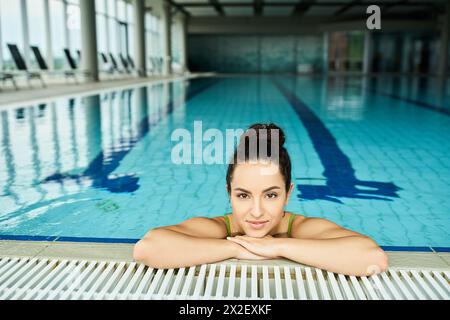 A stunning brunette woman, clad in a swimsuit, striking a pose in a serene indoor pool setting. Stock Photo