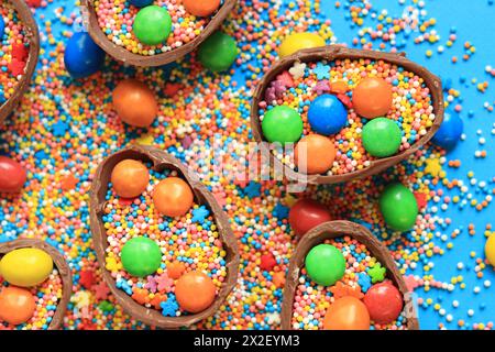 Chocolate eggs with candies and sugar colored sprinkles on a blue background, top view. Easter composition. Halves of chocolate eggs on the table. Fes Stock Photo