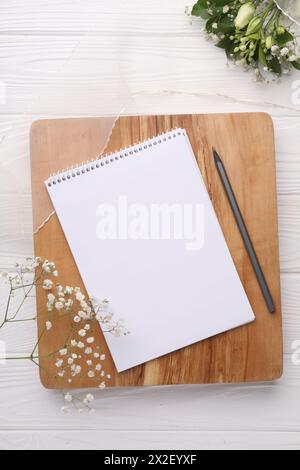 Guest list. Notebook, pencil, beautiful flowers and ribbon on white wooden background, flat lay Stock Photo