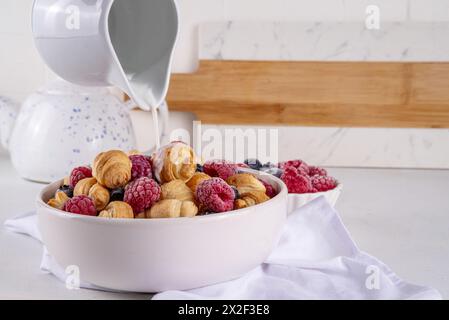 Tiny breakfast croissants cereals with fresh berries and milk. Bowl portions with trendy fresh baked mini petite croissants with raspberry and blueber Stock Photo