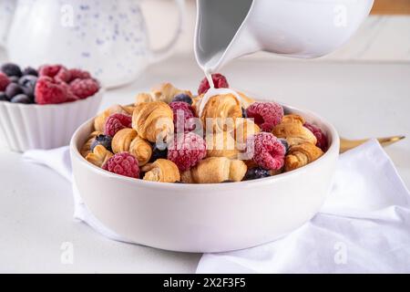 Tiny breakfast croissants cereals with fresh berries and milk. Bowl portions with trendy fresh baked mini petite croissants with raspberry and blueber Stock Photo