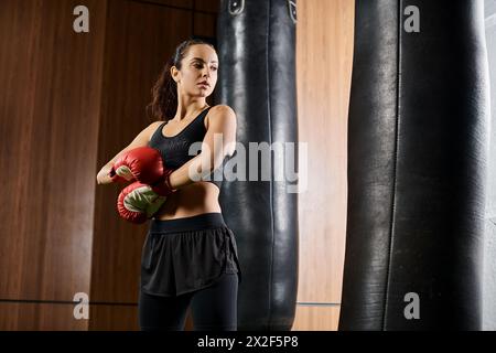A brunette sportswoman in active wear throws punches with red boxing gloves in a gym setting. Stock Photo