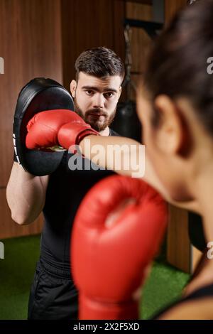 A woman in a black shirt and red boxing gloves practices boxing in a gym. Stock Photo
