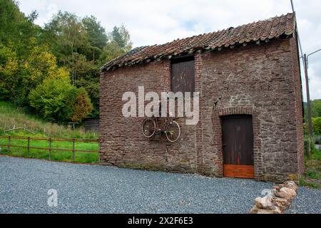 Rusty old bicycle hangs on the side of a barn Photographed in the Ardennes, Belgium Stock Photo