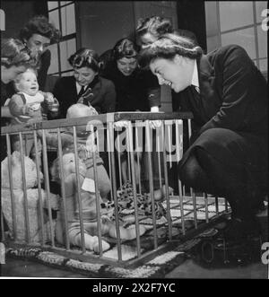 WRENS LEARN MOTHERCRAFT: MEMBERS OF THE WOMEN'S ROYAL NAVAL SERVICE RECEIVE TRAINING FROM THE MOTHERCRAFT TRAINING SOCIETY, LONDON, ENGLAND, UK, 1945 - A group of women of the WRNS, receiving training from the Mothercraft Training Society, talk to three children in a play pen. A large teddy bear is also visible in the play pen. This photograph was probably taken at the MTS headquarters in Highgate Stock Photo