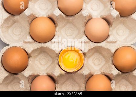 Brown chicken eggs in carton container. One broken egg in container. Flat lay Stock Photo