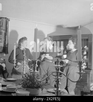 LANDGIRL'S DAY: EVERYDAY LIFE AND AGRICULTURE IN WEST SUSSEX, ENGLAND, UK, 1944 - 29 year old Land Girl Rosalind Cox (centre) and her colleagues enjoy an evening of coffee, sandwiches and gossip in the candle-lit interior of 400 year old Prattendens Cottage in Bury, West Sussex. The cottage was occupied by the radio star Mabel Constanduros before the war. These get-togethers occur every Monday evening, giving the Land Girls the opportunity to relax and talk to one another Stock Photo