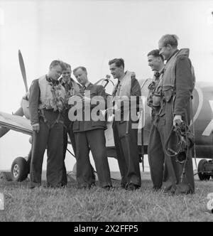 AMERICANS IN BRITAIN: THE WORK OF NO 121 (EAGLE) SQUADRON RAF, ROCHFORD, ESSEX, AUGUST 1942 - An intelligence officer collects information from an Eagle Squadron Spitfire crew after a flight. Left to right, they are: Flying Officer K M Osbourne, Flight Lieutenant Seldon R Edner, the intelligence officer, Squadron Leader W R Williams DFC (the Commanding Officer), Pilot Officer Don A Young and Pilot Officer F R Boyles Royal Air Force Stock Photo