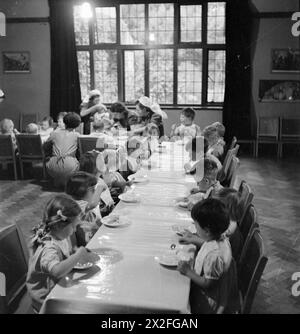 NURSERY FOR WORKING MOTHERS: THE WORK OF FLINT GREEN ROAD NURSERY, BIRMINGHAM, 1942 - Children at the Flint Green Road Nursery enjoy a hearty breakfast of porridge and milk. Toddlers eat at the side table whilst smaller babies eat at the top table, assisted by nurses Stock Photo