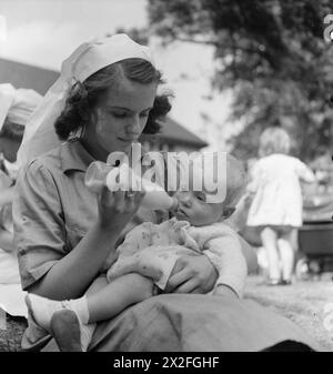 NURSERY FOR WORKING MOTHERS: THE WORK OF FLINT GREEN ROAD NURSERY, BIRMINGHAM, 1942 - A young nurse bottle feeds a baby in the evening sunshine in the grounds of Flint Green Road Nursery Stock Photo