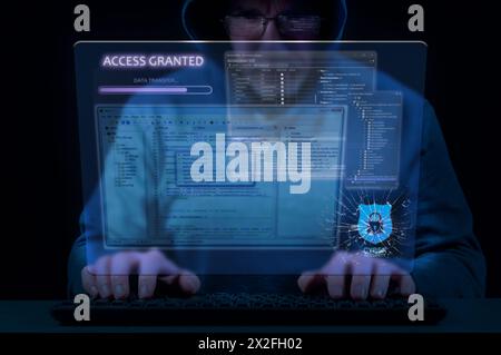 Man in hood on dark background uses keyboard and virtual screen to break cybersecurity system Stock Photo