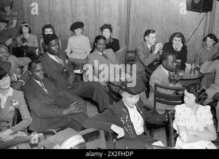 EMPIRE - AND WORLD - PARTY: RADIO BROADCAST FROM THE OVERSEAS CLUB, ST JAMES'S LONDON, 1942 - Technicians from West Africa are amongst those enjoying the broadcast from the Hall of India at the Overseas Club in London. Many civilian women can also be seen sitting around tables to listen to the music and quiz Stock Photo