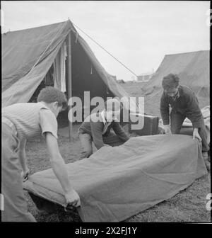 YOUTH SERVICE VOLUNTEERS HELP BRITISH FARMERS: AGRICULTURAL CAMP AT NUNNEY CATCH, SOMERSET, ENGLAND, UK, 1943 - Three boys make their beds at the Youth Service Volunteer camp at Nunney Catch, in between breakfast and work parade. Left to right, they are: Javier Sanchez (aged 16 1/2), Venanchio Zornova (aged 14) and his brother Mario Zornova (aged 16). All were refugees from the Spanish Civil War, and are on holiday from boarding school. The beds are being made outside the tents, which can be seen behind the boys as they work Stock Photo