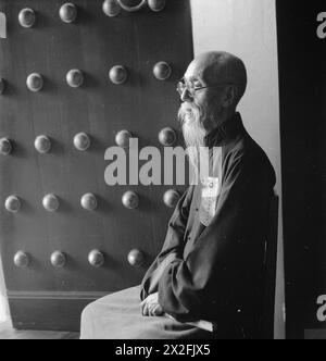 Cecil Beaton photographed scholar and former Minister of the Interior Chow Chung-yuch seated next to a studded door in China, 1944, highlighting formal attire and interior architecture. Stock Photo